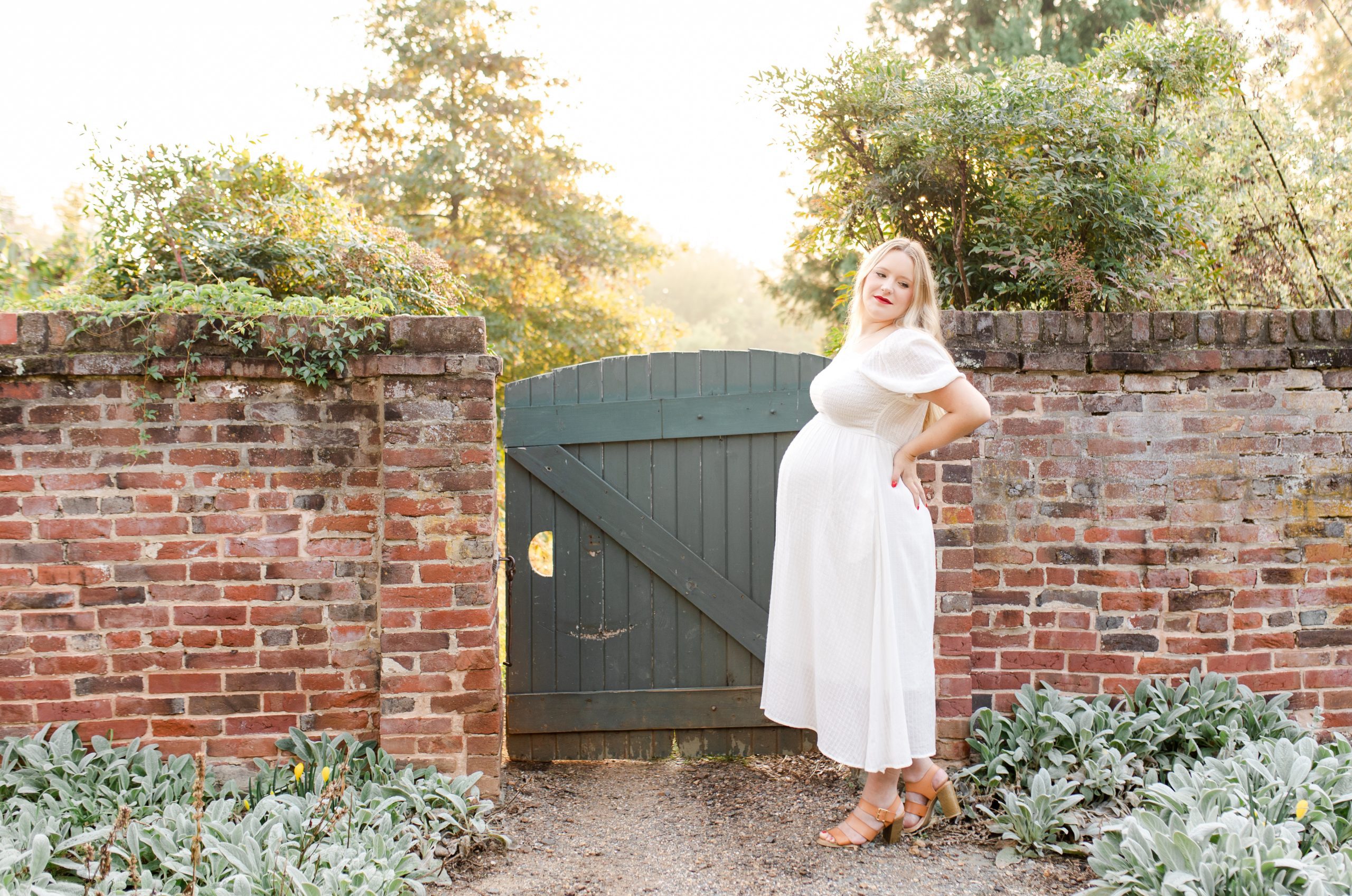 mom-to-be standing in a garden near a brick wall with a gate by Northern Virginia Maternity Photographer