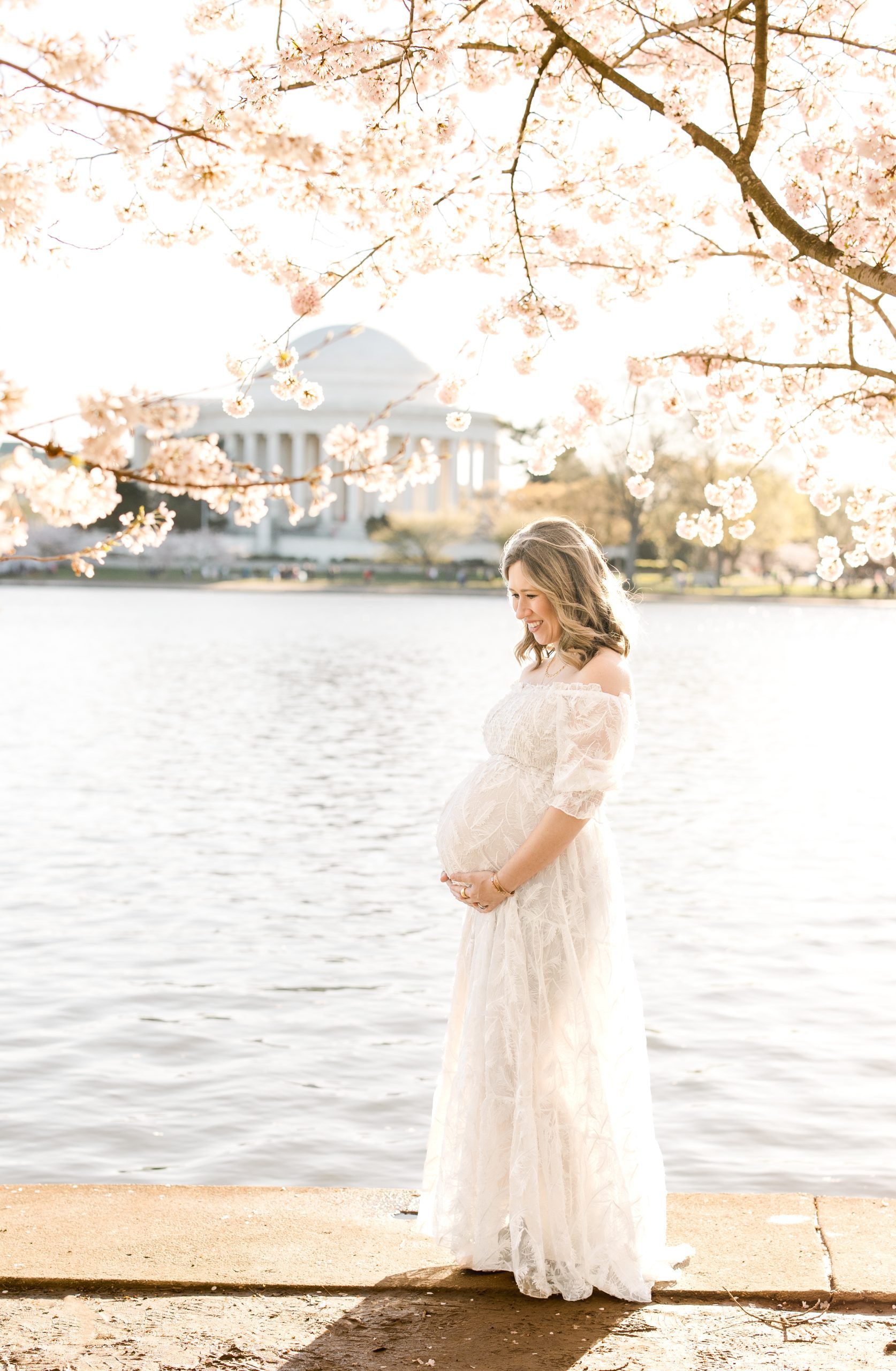 Full length shot of a Mom-to-be in a white feathered dress at the Tidal Basin for a Cherry Blossom Maternity Session