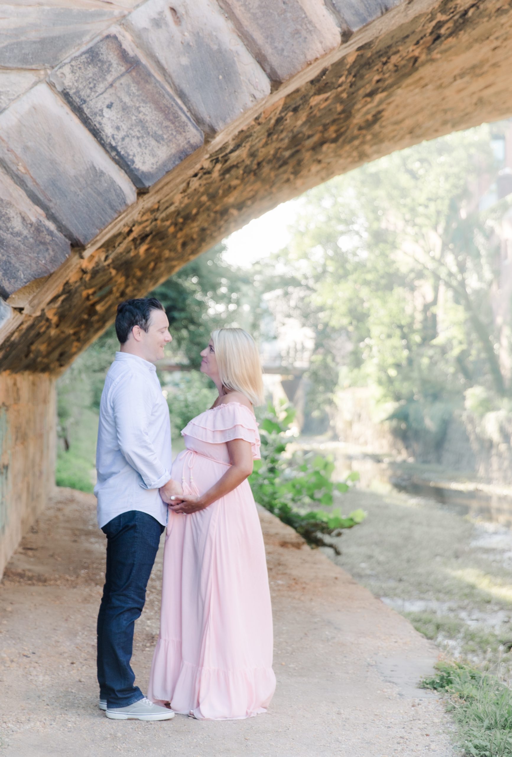 dad and mom-to-be posed near a stone bridge by the canal in Georgetown by northern virginia maternity photographer