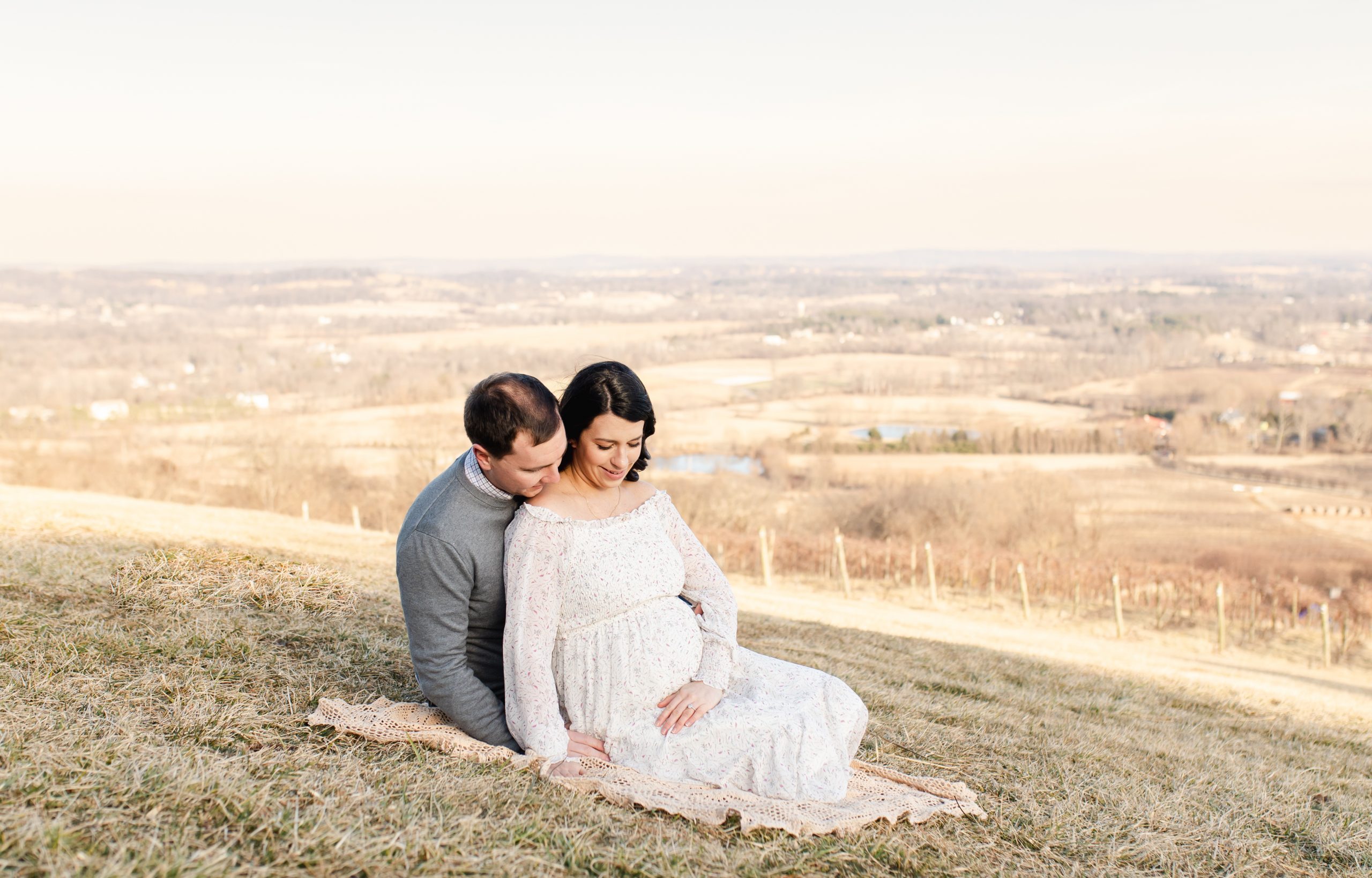 dad and mom-to-be sitting up on a hill overlooking bluemont vineyard in virginia by Northern Virginia Newborn Photographer