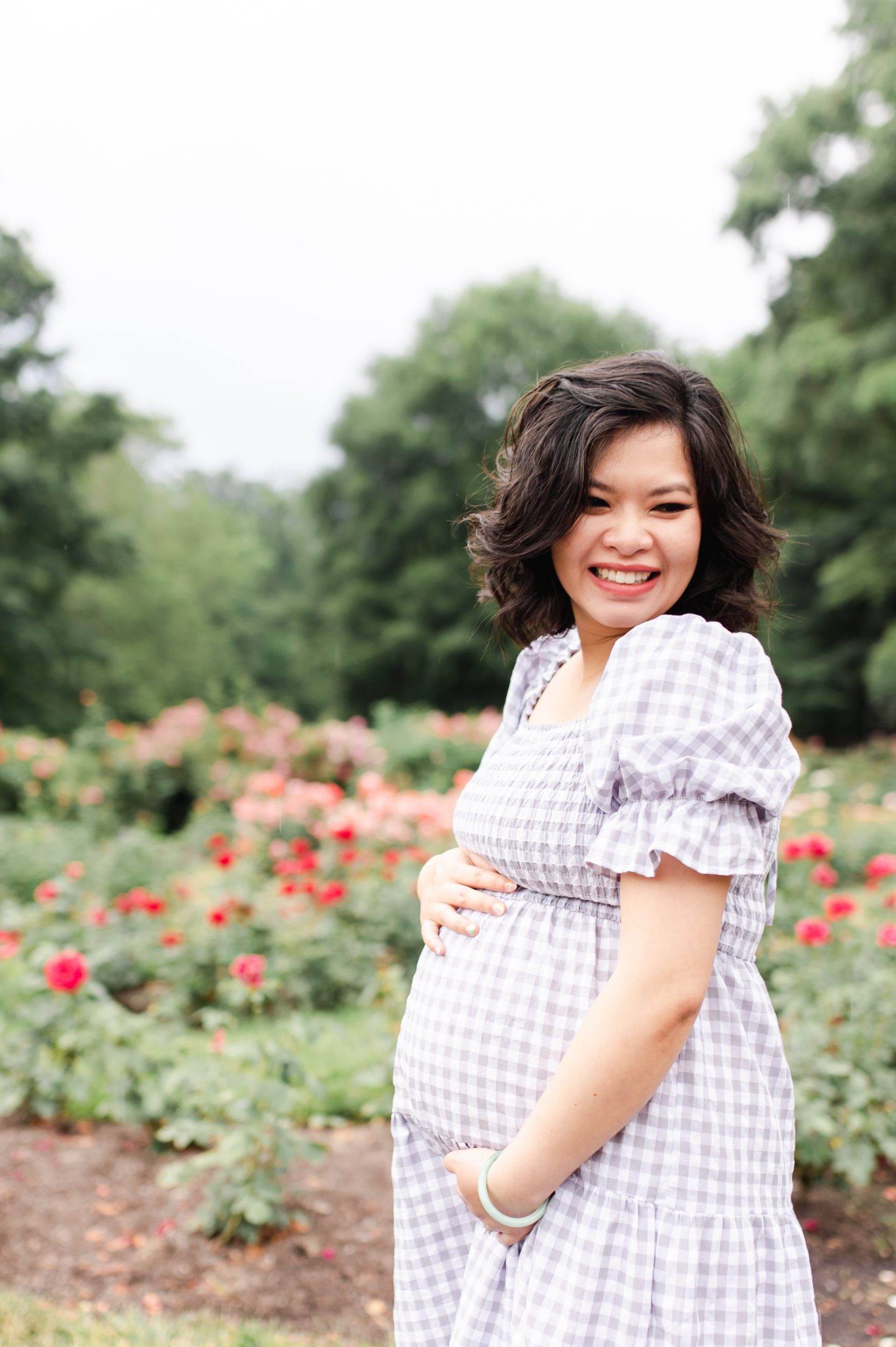 mom-to-be smiling and cradling bump amongst the roses at bon air park in arlington va by northern virginia maternity photographer