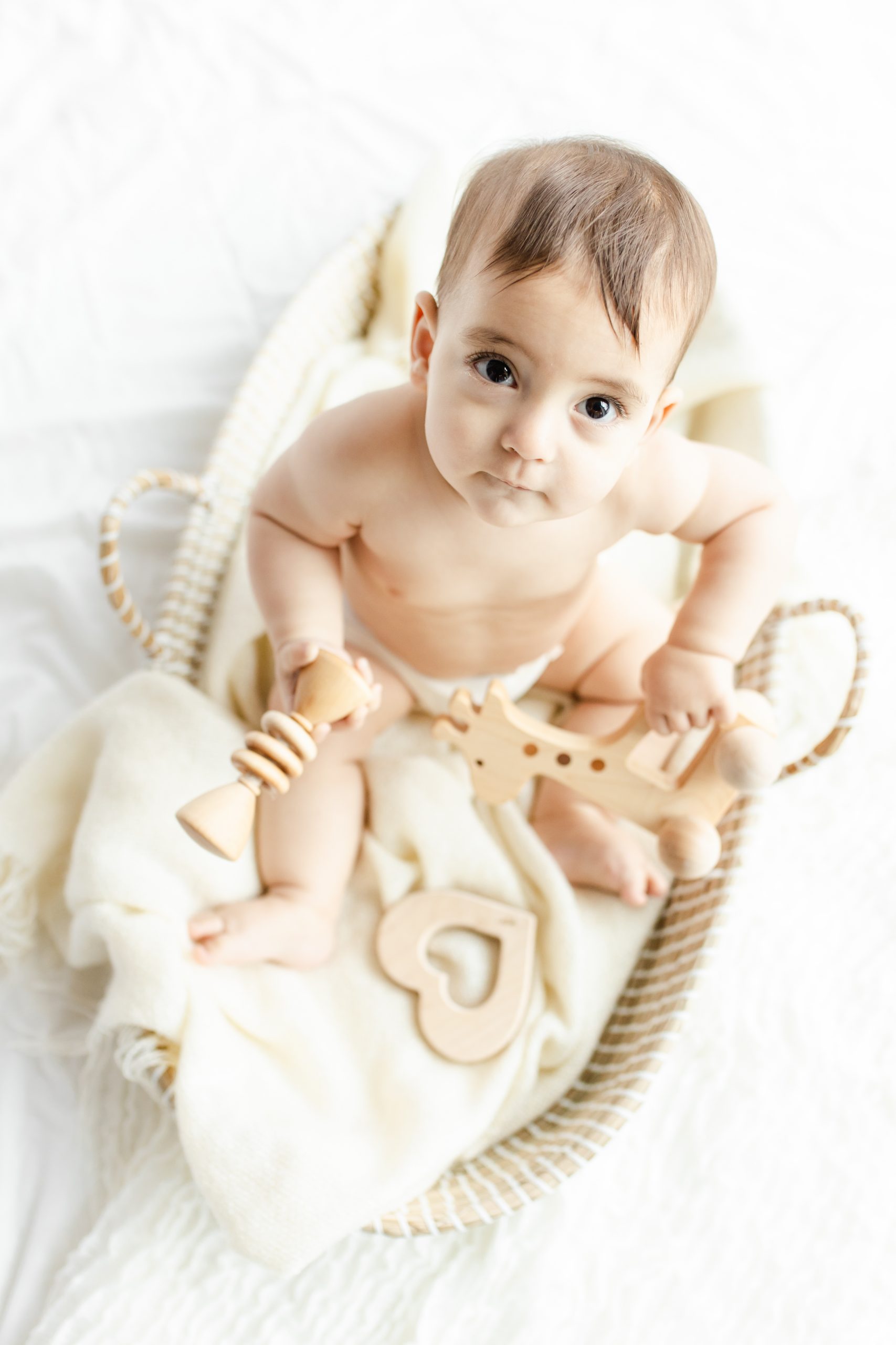 baby sitting in a basket, wooden toys in his hands, looking up at the camera by Northern Virginia Baby Photographer