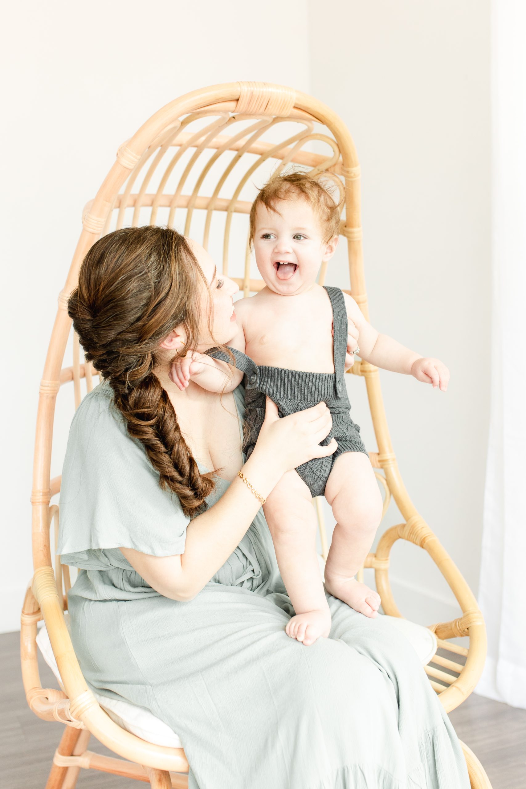 mom sitting in chair with her baby standing on her lap smiling by northern virginia baby photographer