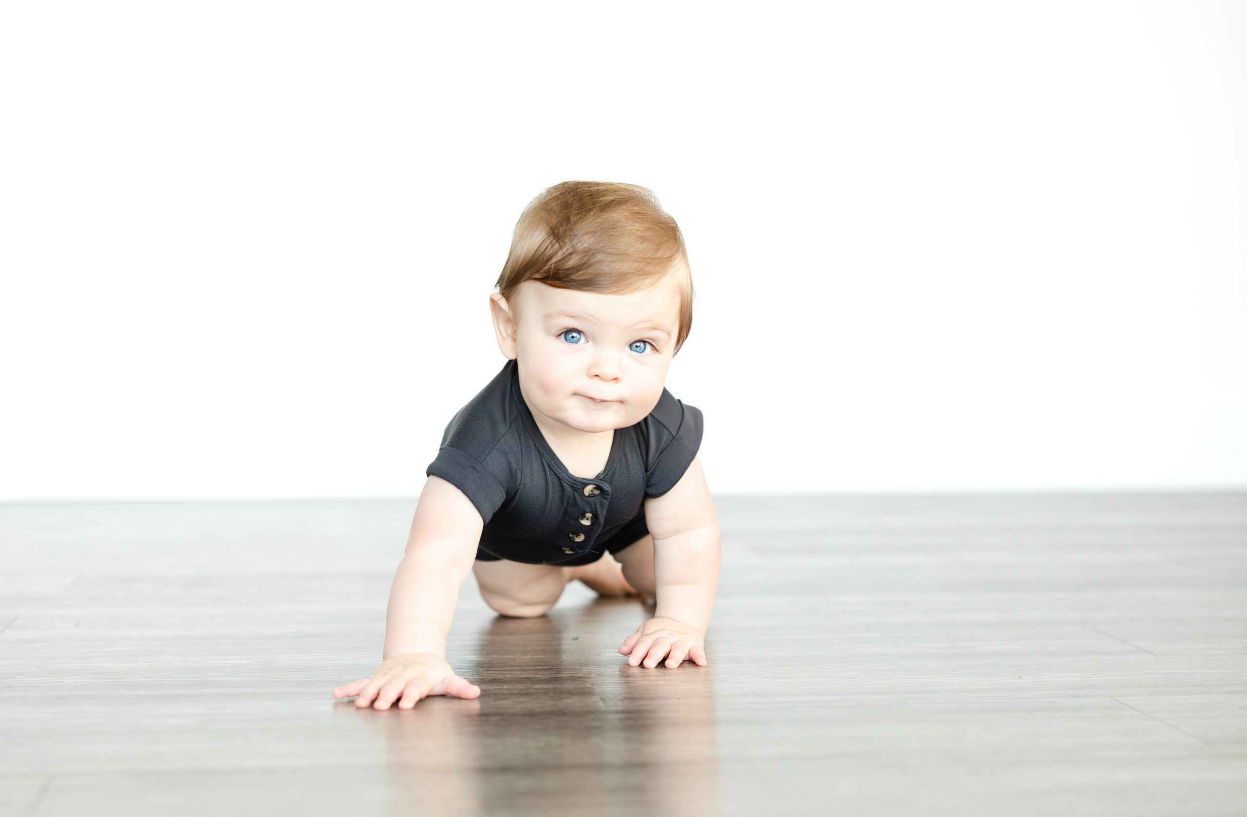 Portrait of a one year old boy with blue eyes crawling towards the camera at a studio in Leesburg, VA.
