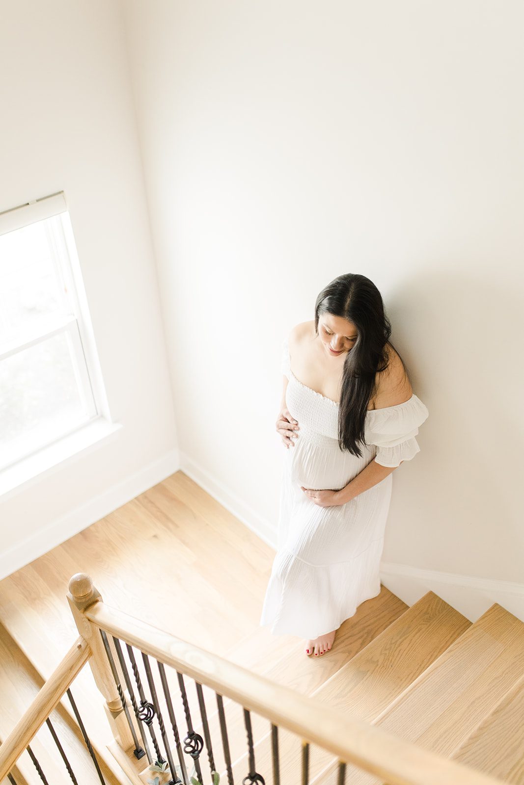 expecting mom posing in the stairwell of her home at an in-home maternity session.