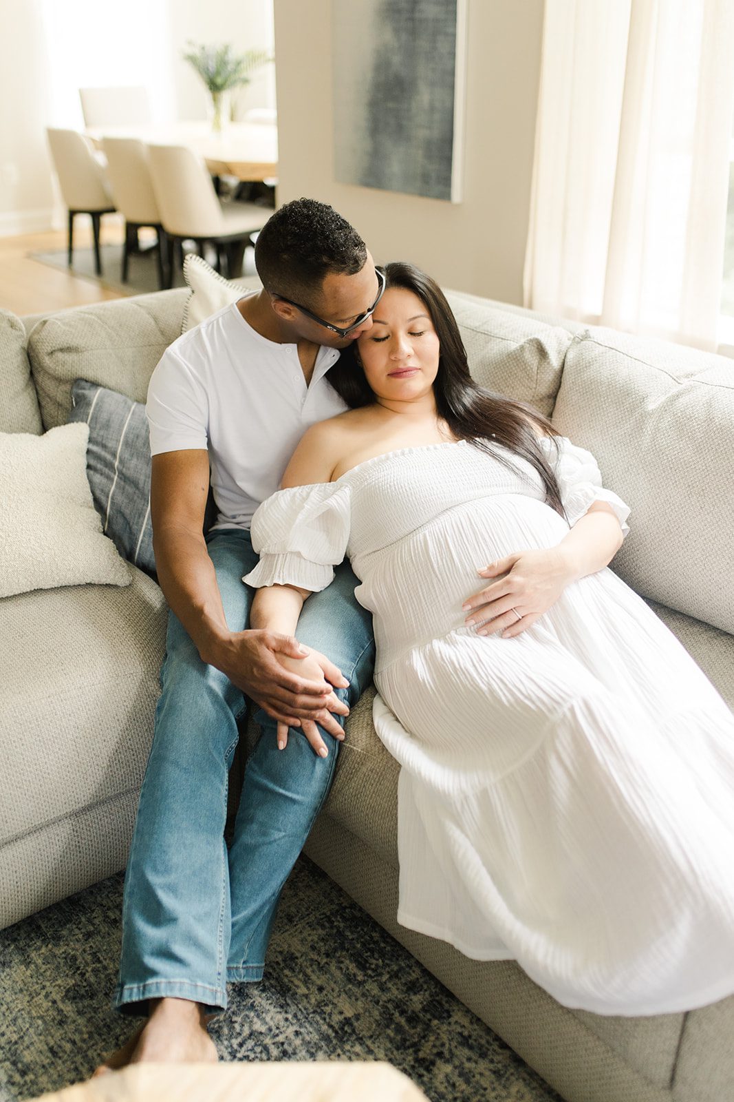 expecting parents snuggled close on the couch in their living room during an in-home maternity session