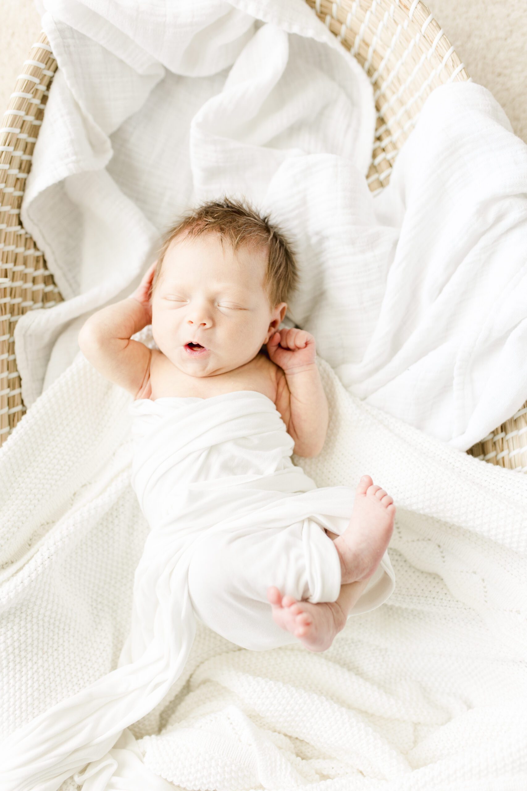 newborn baby girl stretching out in a woven basket