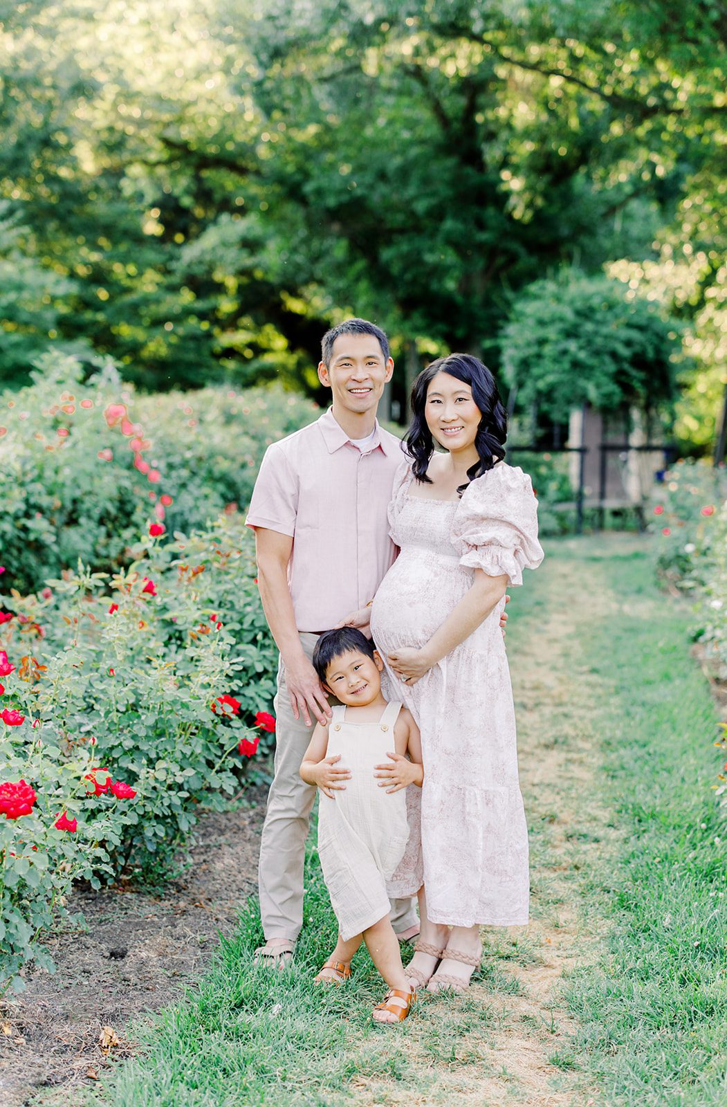 Happy pregnant mom and dad stand in a garden with their toddler son smiling before visiting baby shower venues in DC
