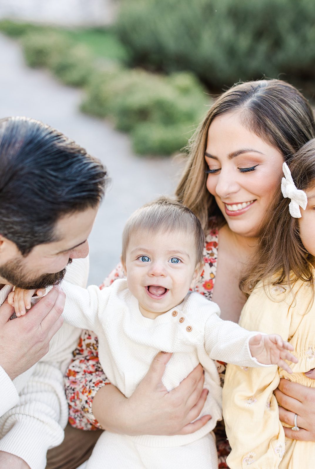 A happy baby smiles and reaches out while sitting in mom's arms and holding dad's hand during toddler activities in Washington DC