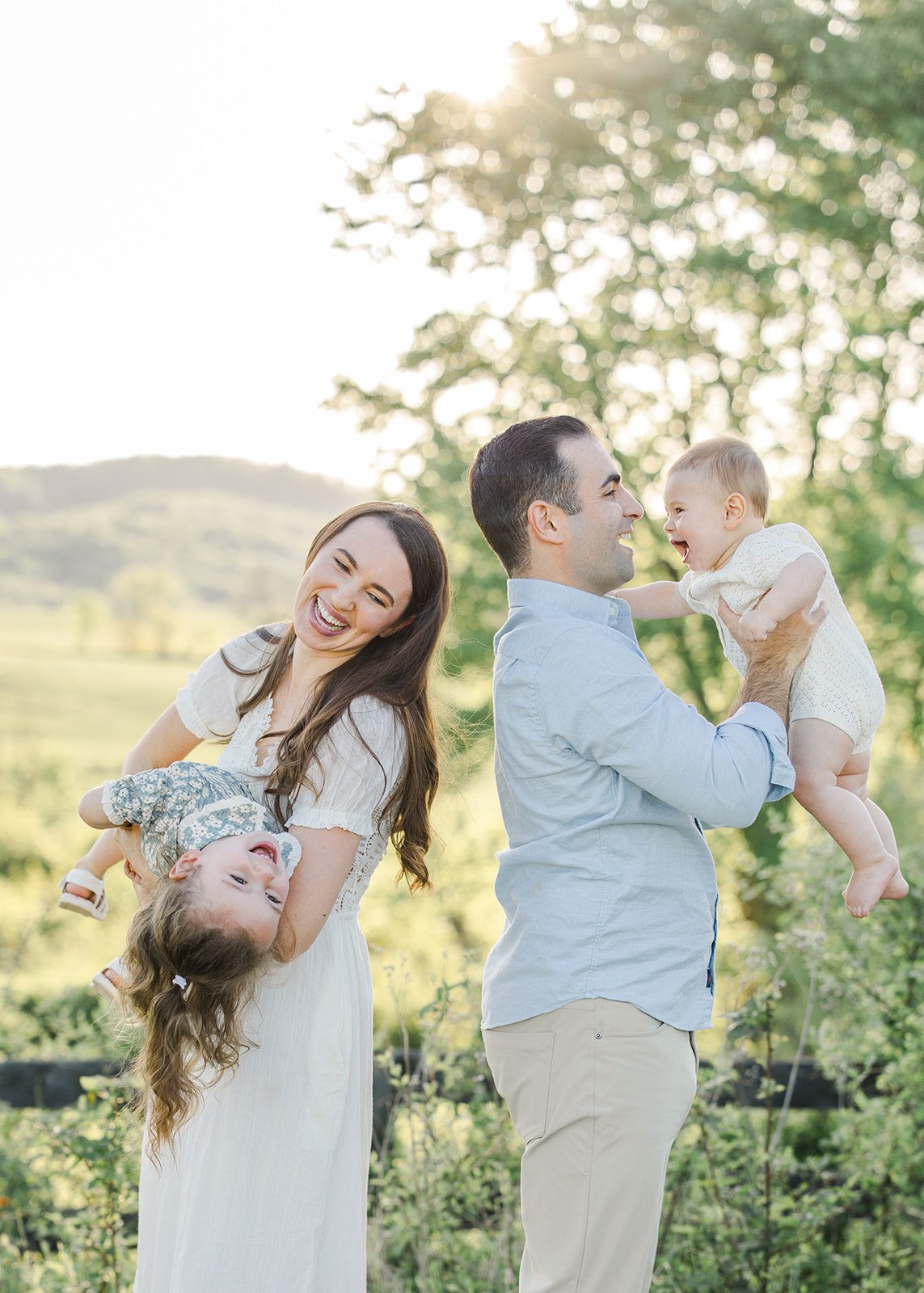 mom holding toddler upside down and dad holding smiling baby